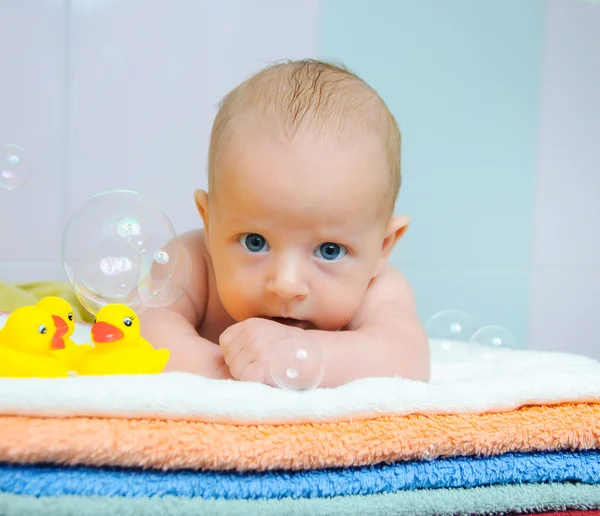 Pequeno menino bonito com bolhas de sabão deitado em toalhas coloridas — Fotografia de Stock