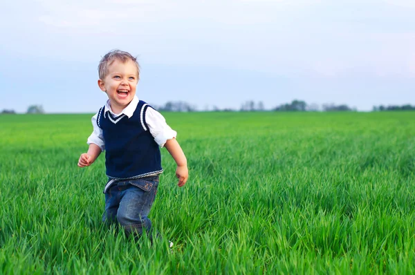 En vacker liten pojke runing i gräset — Stockfoto