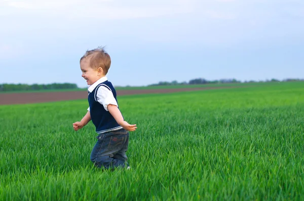 En vacker liten pojke runing i gräset — Stockfoto