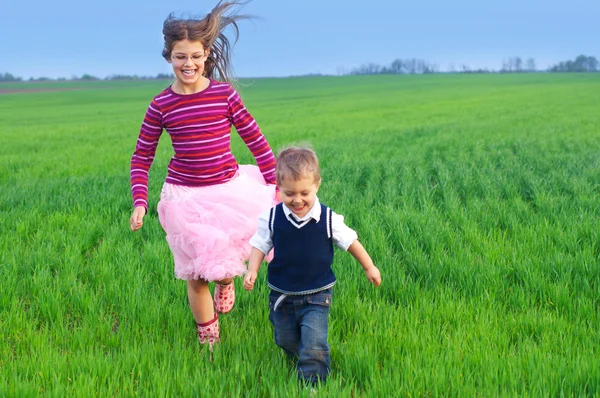 Zuster runing met haar brather op het gras — Stockfoto