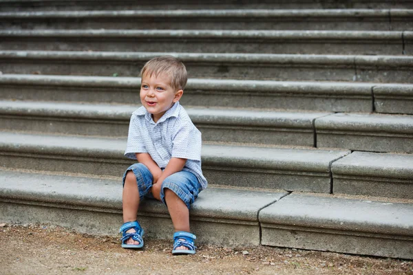 Kisfiú ül a parkban a lépcsőn — Stock Fotó