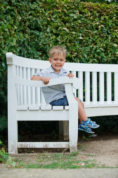 Liten pojke sitter på en bänk i en park — Stockfoto