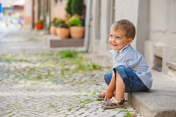 Little boy sits on the doorstep on a city street — Stock Photo, Image