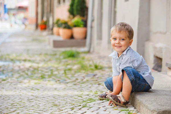 Kleine jongen zit op de deur op een stad straat — Stockfoto