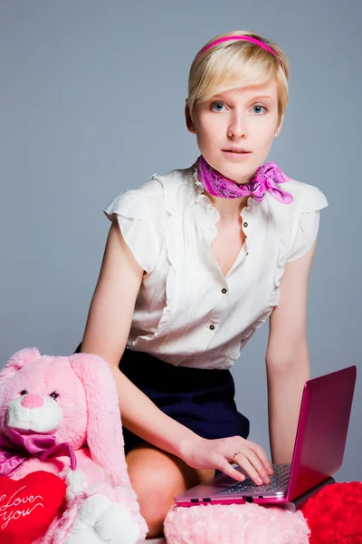Prachtige blond meisje werken met roze laptop — Stockfoto