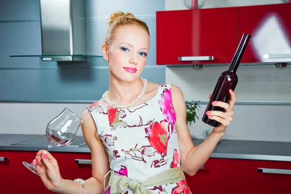 Blond meisje met glas en fles met wijn in interieur van rode keuken — Stockfoto