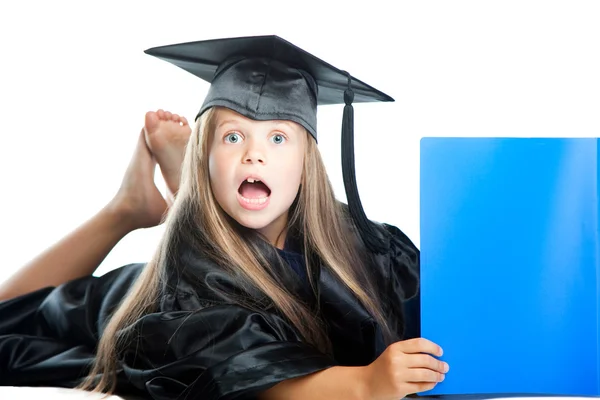 Linda niña en vestido de graduación con libro azul en blanco aislado — Foto de Stock