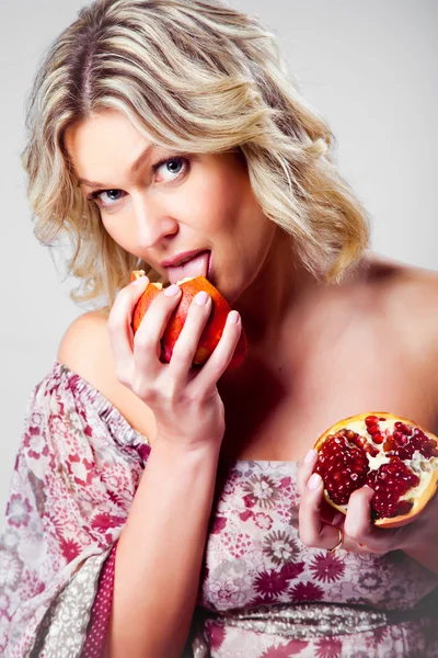Blonde woman licking pomegranate on grey — Stock Photo, Image