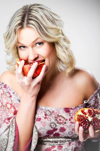 Blonde vrouw granaatappel bijten op grijs — Stockfoto