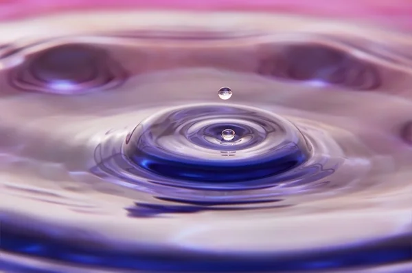 Dos pequeñas gotas de agua cayendo sobre la superficie colorida del agua —  Fotos de Stock