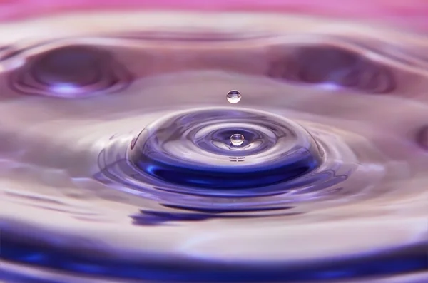 Zwei kleine Wassertropfen fallen auf die bunte Wasseroberfläche — Stockfoto