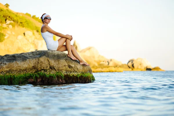 Женщина, сидящая на камне в море — стоковое фото