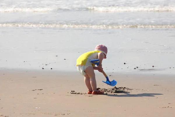 stock image Young child playing with a shovel on the sand of the beach