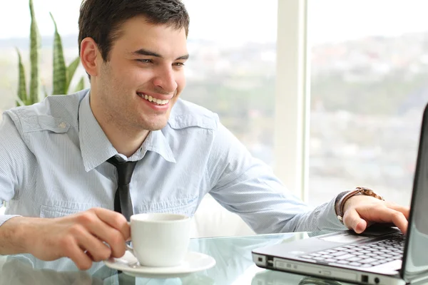 Young man with cup looking at the laptop — Stock Photo, Image