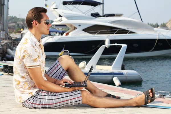 Handsome businessman running a laptop on the shore near the yach — Stock Photo, Image