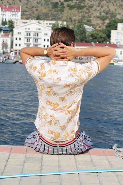 Knappe man ontspannen, zittend op de pier in de buurt van zee, op zoek op — Stockfoto