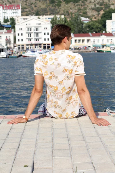 Красивий чоловік розслабляється, сидить на причалі біля моря, чекаючи — стокове фото