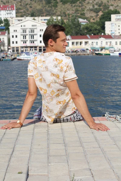 Bonito homem relaxante, sentado no cais perto do mar, olhando — Fotografia de Stock