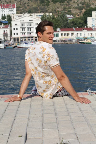 Handsome man relaxing, sitting on the pier near sea, looking awa — Stock Photo, Image