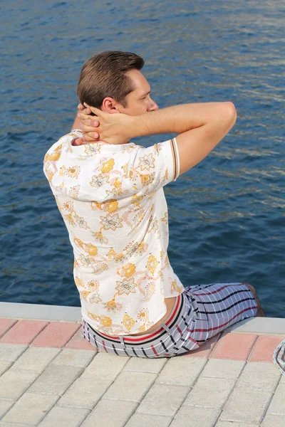 Knappe man ontspannen, zittend op de pier in de buurt van zee, op zoek awa — Stockfoto
