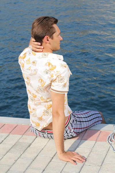 ハンサムな男、ビーチでリラックス、桟橋の上に座って、探しています — ストック写真