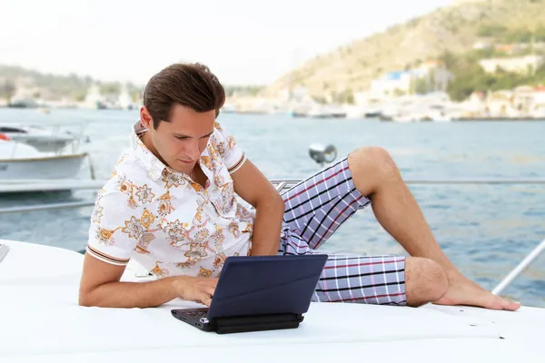 Stilig affärsman liggande på en yacht och arbetar på en bärbar dator — Stockfoto
