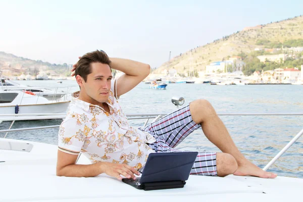 英俊的商人正躺在一艘游艇上和便携式计算机上工作 — 图库照片