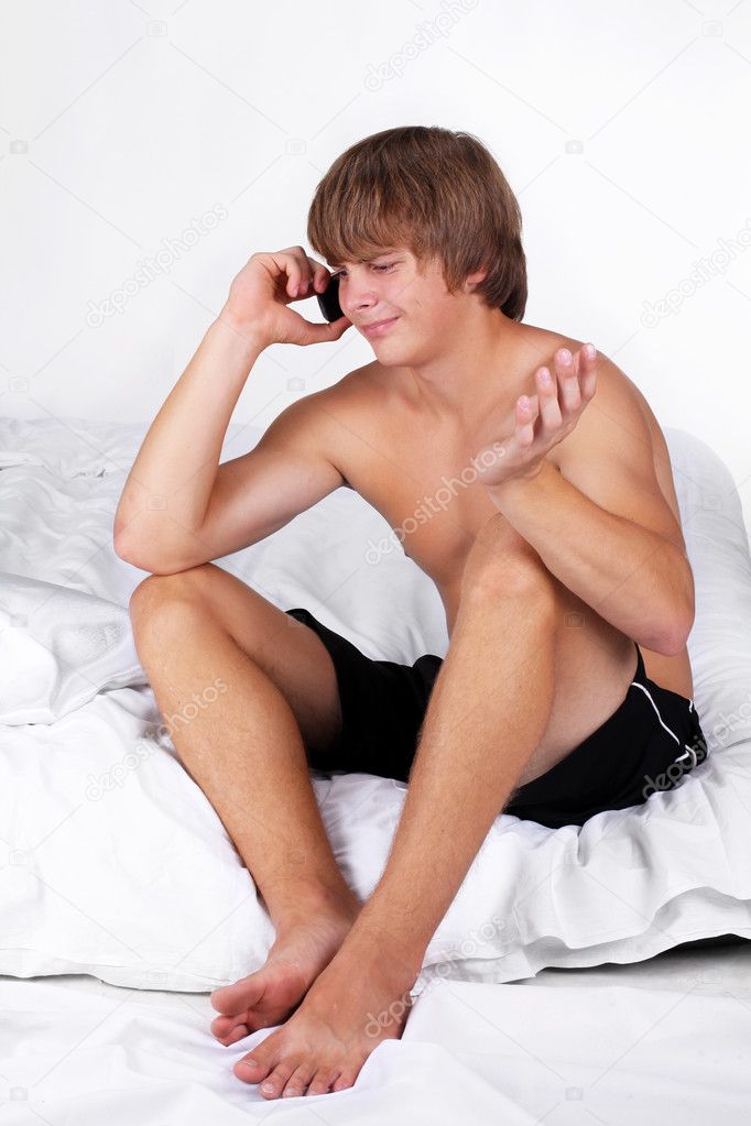 Young guy in white bed talking on mobile phone, emotions