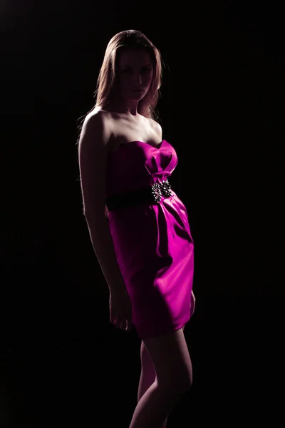 Žena v růžových šatech na tmavém pozadí, tmavé stíny — Stock fotografie