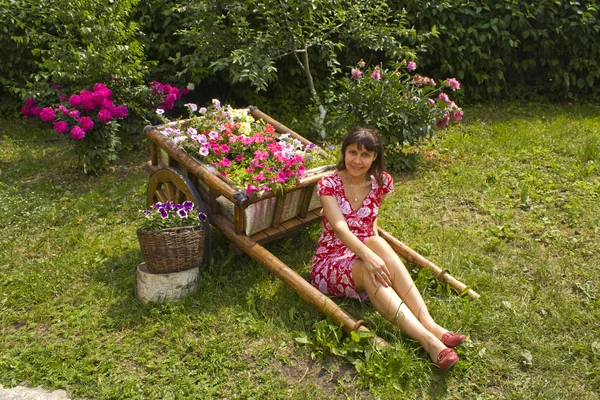 Girl sitting in the garden near carriage with flowers — Stock Photo, Image