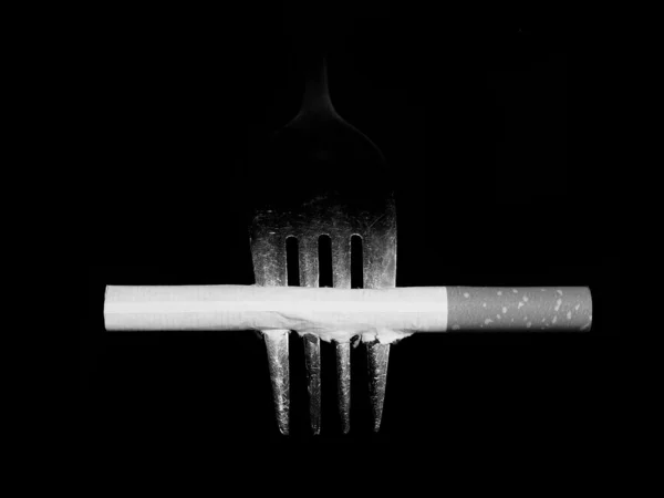 Konzept schwarze weiße Zigarette und Gabel isoliert auf schwarzem Hintergrund — Stockfoto