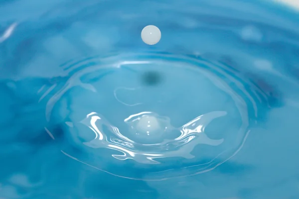 Goccia di latte che colpisce l'acqua blu — Foto Stock