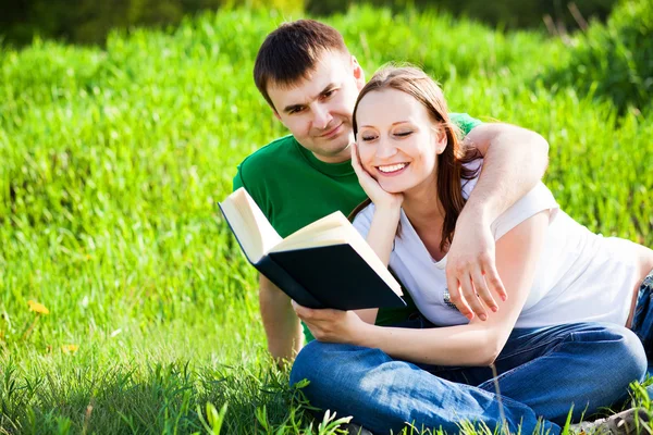 Couple sitting in park reading book — Stock Photo, Image