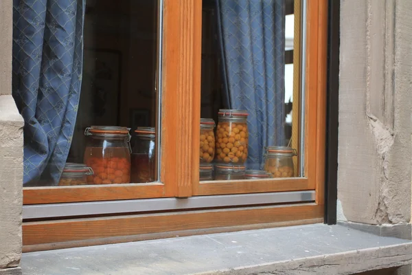 stock image Window with blue curtaiins and jars of mirabell plums