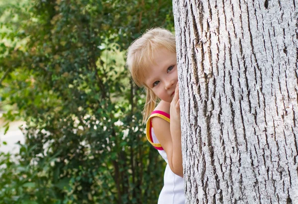 Menina bonita escondida atrás de uma árvore — Fotografia de Stock