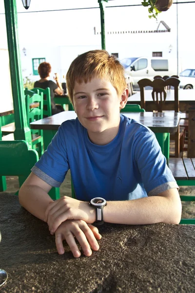 Le jeune garçon est assis sur une table dans un restaurant — Photo