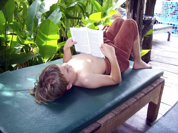 Boy reading a book while relaxing on a wooden couch — Stock Photo, Image