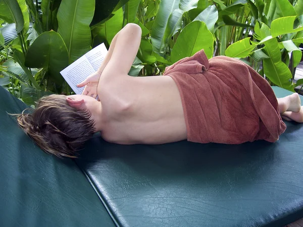 Junge liest ein Buch während er es sich auf einer Holzcouch gemütlich macht — Stockfoto