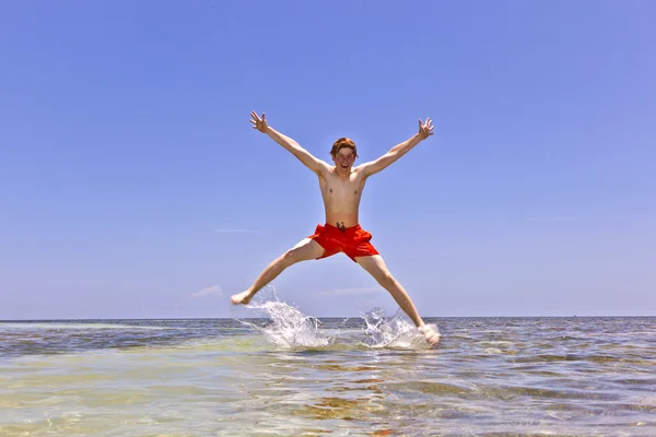 年轻的男孩跳出来的水在热带海滩 — 图库照片