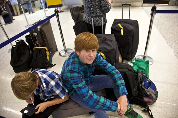 Jungen sitzen auf dem Gepäckstück und warten auf den Check-in am Flughafen — Stockfoto