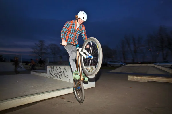 Menino em sua dirtbike pulando no parque de skate à noite — Fotografia de Stock