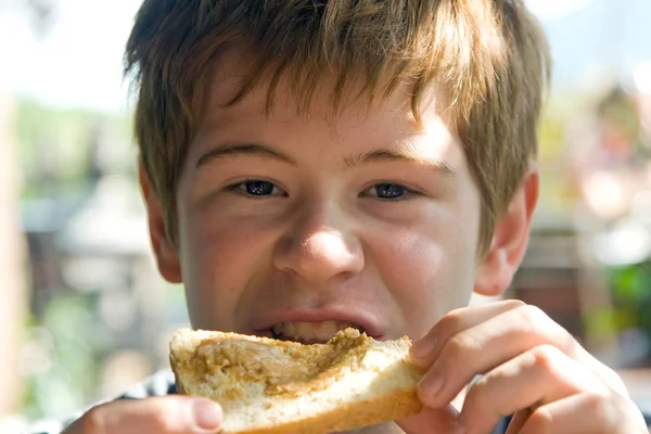 Joung menino está comendo torradas com creme no topo, desfrutando de refeição — Fotografia de Stock