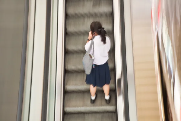 Estudiante en la escalera móvil en el vestido de la escuela usando el móvil —  Fotos de Stock