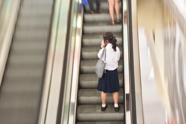 Student på moving trappan i skolan klänning med mobilen — Stockfoto