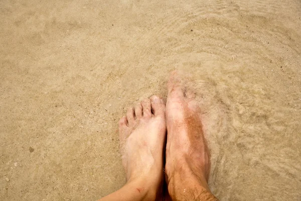 Pies de un hombre en la arena fina rodeado de agua salada — Foto de Stock