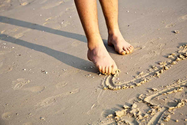 Los pies de un niño está pintando figuras en la arena fina de la beauti —  Fotos de Stock