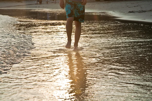 Feed van man op het water lopen in het strand in achtergrondverlichting — Stockfoto