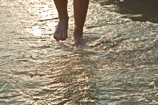 Feed van man op het water lopen in het strand in achtergrondverlichting — Stockfoto