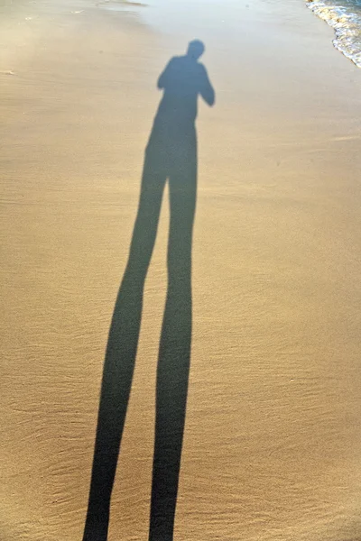 Довга тінь чоловіка у дрібному піску пляжу, ноги — стокове фото
