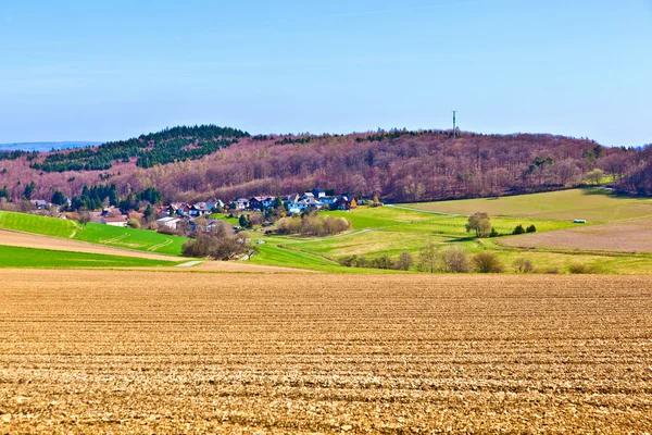 Paisagem com campos e uma aldeia com colinas no horizonte — Fotografia de Stock